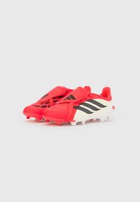 Κόκκινα και λευκά ποδοσφαιρικά παπούτσια Adidas Predator με μαύρες ρίγες και καλυμμένα κορδόνια, τοποθετημένα δίπλα το ένα στο άλλο σε λευκό φόντο.