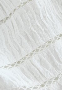 Tissu blanc texturé avec des plis verticaux et une dentelle en bordure. Le matériau semble transparent avec un léger effet froissé.