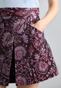 Sötét bordó színű, virágmintás szoknya világoskék és rózsaszín díszítéssel, ráncolt fazonnal és oldalsó zsebekkel.