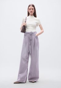 Φαρδύ παντελόνι λιλά με πιέτες και ψηλή μέση, συνδυασμένο με εφαρμοστή κρεμ ριμπ μπλούζα με κοντά μανίκια. Καφέ τσάντα ώμου.