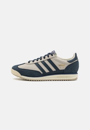 Sneaker in suede blu e pelle beige con tre strisce scure, suola di gomma crema e tomaia perforata per la ventilazione. Design classico.