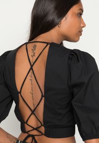 Top cropped preto com mangas bufantes e um design de costas em crisscross com cordão. Tecido liso, sem padrões visíveis ou detalhes em metal.