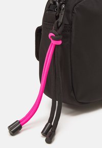 Borsa in tessuto nero con un cordino nero e rosa. Il cordino rosa è più spesso e rifinito con punte in plastica per la chiusura.