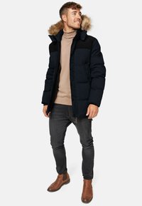 Sort pufferjakke med en aftagelig faux fur hætte, der har lynlås- og knaplukning, sidelommer og et farveblokeret design.