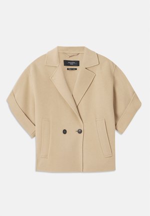 Chaqueta beige de corte cruzado con mangas cortas, que presenta un cuello con muescas y dos bolsillos frontales, confeccionada en una suave tela texturizada.