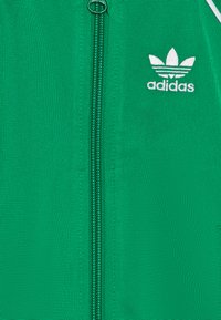 Casaco verde com fecho éclair, feito de tecido texturizado, apresentando um fecho central, logótipo Adidas branco e detalhes em branco contrastantes.