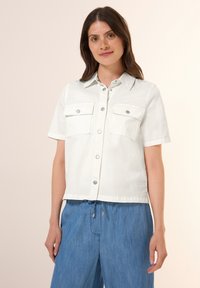 Camicia bianca a maniche corte, in un tessuto strutturato, con due tasche sul petto e bottoni a pressione argentati per la chiusura.