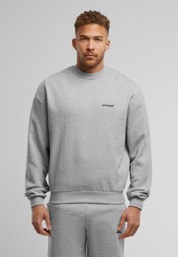 Grijze sweatshirt met een ronde hals, lange mouwen en geribde manchetten. Bevat een klein zwart "UPGRADE" logo op de linkervoorzijde. Zachte textuur.