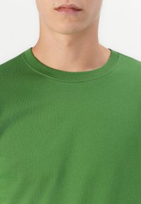 Green cotton t-shirt with a crew neckline. The fabric has a smooth texture and a solid color without patterns or accents.