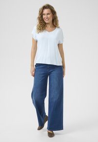 Blouse rayée bleu clair avec un col en V et des manches courtes, associée à un jean en denim foncé à jambes larges et des ballerines marron. Design simple et décontracté.