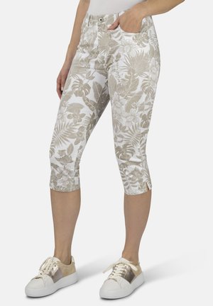 Blumenmuster, gekürzte Hose in Beige und Weiß, aus leichtem Stoff. Mit seitlichen Taschen und einem gesäumten Saum. Kombiniert mit weißen Sneakers.