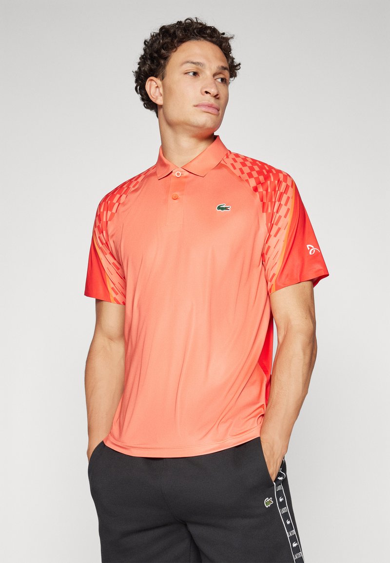 Kurzärmliges Poloshirt in leuchtendem Koralle mit glattem Material, einem Kragen und gemusterten Ärmeln sowie einem Logo auf der Brust.