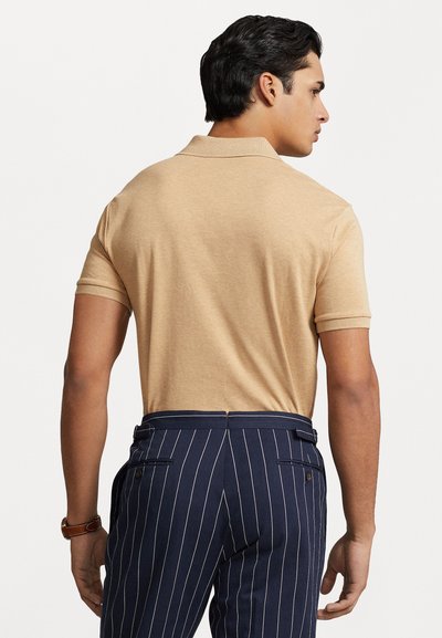 Beige polo särk lühikeste varrukatega, sile tekstuur, kantud tumesiniste triibuliste pükstega, millel on kohandatud lõige ja tasku üksikasjad.