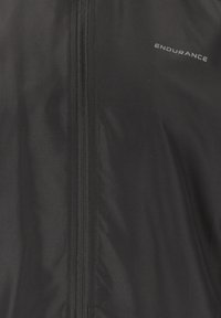 Svart idrottsjacka i lätt, strukturerad tyg. Har dragkedja och "ENDURANCE"-logotypen på övre vänstra sidan.