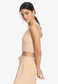 Beige ribbed crop top with thin straps, featuring a fitted design and a seamless finish, paired with matching loose-fit pants.