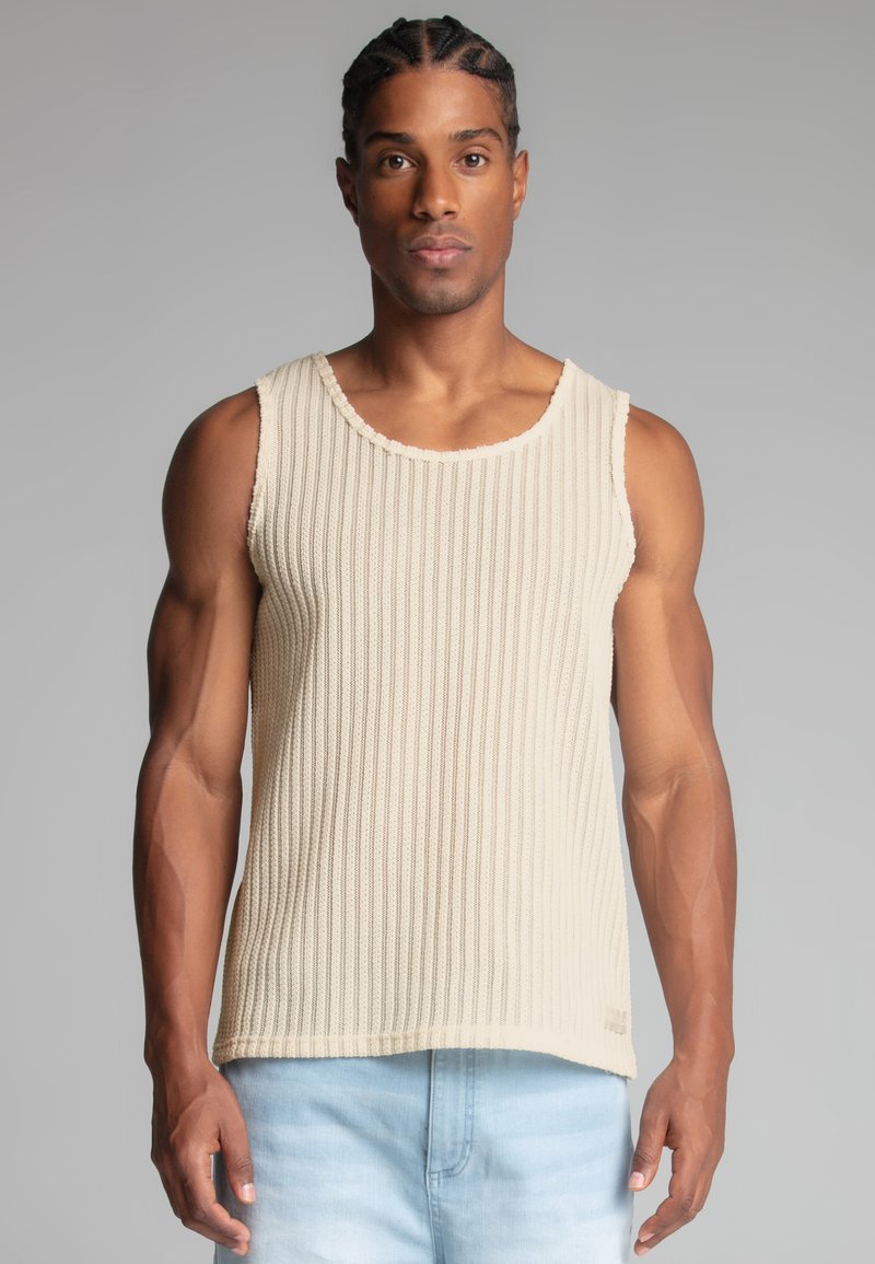 Top sin mangas de punto beige con textura en relieve, escote redondo y acabados sin rematar. Combinado con jeans de color azul claro.