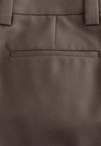 Close-up of brown fabric pants showing back pocket and belt loops with visible stitching and texture.