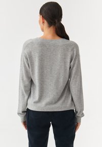 Grijze gebreide trui met een ontspannen pasvorm, ronde halslijn en lange mouwen. De stof heeft een zachte textuur, gecombineerd met donkerblauwe broek.