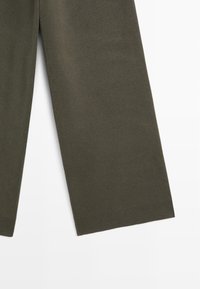 Pantalon à jambes larges de couleur vert olive foncé, confectionné dans un tissu doux à la texture lisse. Dispose d'un ourlet côtelé en bas pour un détail supplémentaire.