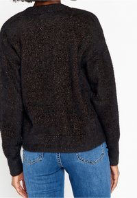 Svart texturerad tröja med metalltråd, med långa ärmar och avslappnad passform. Synlig sömnad vid fållen och ärmänden.