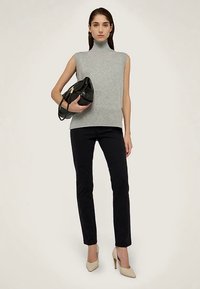 Grå ärmlös polotröja med ribbad fåll, kombinerad med smala svarta byxor och beiga klackar, hålls med en svart handväska.