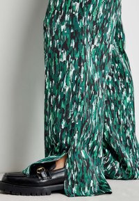 Zielono-czarne spodnie z szerokimi nogawkami i rozcięciami, wykonane z miękkiego materiału. Połączone z czarnymi mokasynami z detalem klamry.