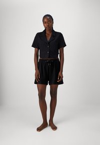 Chemise noire courte à boutons avec un motif texturé ; associée à un short noir avec une taille élastique et un détail de cordon de serrage.