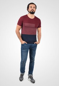 Short-sleeve t-shirt with maroon and navy color blocking, features a chest pocket; paired with blue denim jeans and gray athletic shoes.