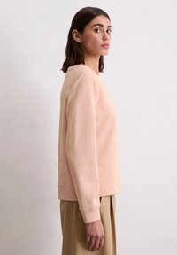 Zachte roze sweatshirt met lange mouwen, een ontspannen pasvorm en geribde manchetten. De stof heeft een gladde textuur en een ronde hals.