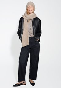 Zwarte leren jas over een licht beige top met knopen, gecombineerd met wijde zwarte broek, een beige gebreide sjaal en een bijpassende muts.