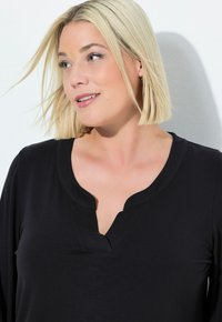 Zwarte top met V-hals ontwerp, lange mouwen, zacht materiaal en een gladde textuur. Simpele en casual stijl zonder zichtbare patronen of accessoires.