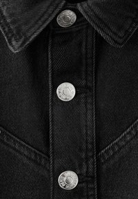 Detail čiernej denimovej bundy s striebornými kovaniami, vrátane gombíkov, špicatého goliera a textúrovaného látky s vertikálnym prešitím.