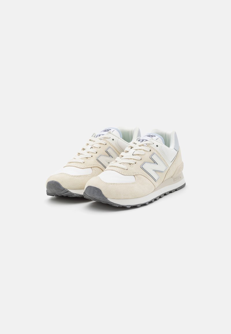Beige Wildlederschuh mit einem weißen Mesh-Obermaterial, grauer Gummisohle und erhabenem 'N'-Logo an der Seite. Verfügt über Schnürsenkel und einen gepolsterten Kragen.