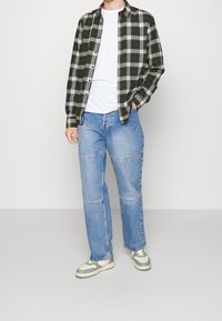 Zeleno-černá kostičkovaná košile přes bílém tričku, spárovaná se světle modrými džíny a teniskami s zelenými akcenty. Uvolněný střih, pohodlný design.