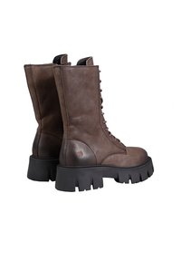 Brown leather combat boots with a high shaft, lace-up front, and thick black rubber sole featuring a toothed edge and logo detail.