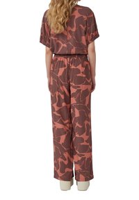 Bordeaux jumpsuit met korte mouwen, elastische tailleband, ruime pasvorm en grote abstracte lichtroze patronen over de stof.