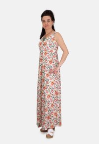 Vestido maxi floral en blanco con un estampado floral multicolor, que cuenta con un escote en V, diseño sin mangas y una silueta fluida. Llevado con zuecos.