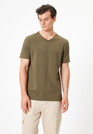 Camiseta de manga corta color verde oliva con escote en V, fabricada en un tejido suave; presenta un corte holgado y un diseño sencillo.