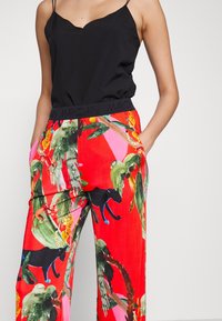 Haut noir sans manches avec encolure festonnée, associé à un pantalon rouge vif orné d'un imprimé tropical d'animaux et de plantes, avec une taille élastique.