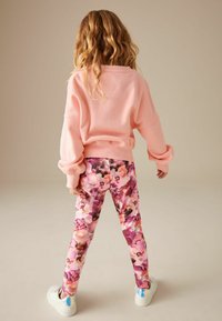 Felpa rosa con maniche voluminose, abbinata a leggings floreali nei toni del rosa e del viola. Sneakers bianche con dettagli metallici.