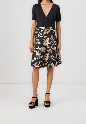 Robe noire avec un décolleté en V profond et des manches courtes, ornée d'un motif floral doré sur une jupe évasée. Associée à des sandales à plateforme noires.