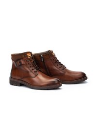 Botas de tobillo de cuero marrón con un acabado suave, que cuentan con cordones y un zipper lateral; punta redondeada y cuello texturizado. Suela de goma resistente.