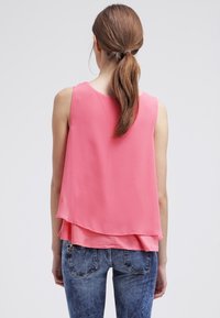 Haut rose sans manches avec un design en couches ; fabriqué en tissu léger ; le dos présente un ourlet incurvé ; associé à un jean en denim bleu.