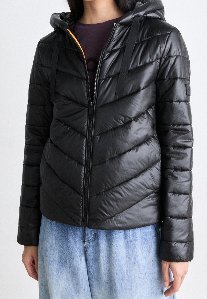 Czarna puchowa kurtka z kapturem, ozdobiona pikowaniem w jodełkę, z zamkiem błyskawicznym z przodu i kontrastowym kolorem wnętrza. Odłączane troczki kaptura.