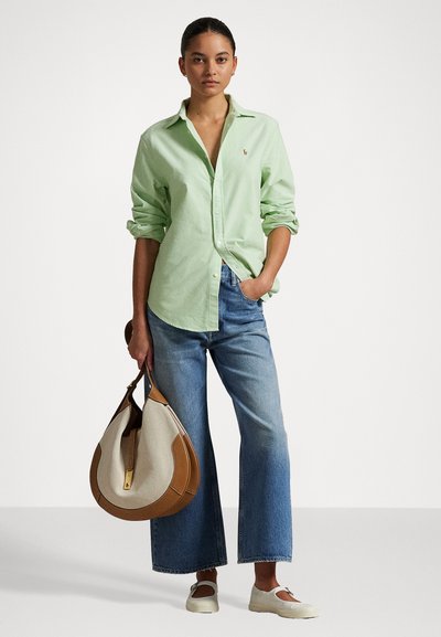 Chemise boutonnière vert clair, jeans larges bleus, chaussures grises à enfiler, et un grand sac à main beige et marron avec un fermoir en or.