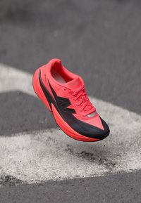 Chaussure de course avec un dessus corail vif, des accents noirs et une forme aérodynamique. Comprend un matériau texturé et un logo de marque visible.