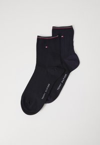 Un par de calcetines en azul marino oscuro y textura estampada. Uno presenta un diseño acanalado; ambos tienen un pequeño logo y un cuello en contraste.