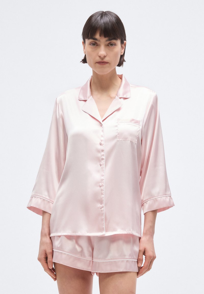 Σετ ροζ σατέν πιτζάμες με πουκάμισο με κουμπιά και μανίκια τριών τετάρτων, συνοδευόμενο από σορτς με δίπλωμα στο τελείωμα.