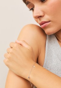 Woman wearing a delicate silver chain bracelet with small star charms, resting her hand on her bare shoulder.