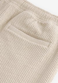 Tissu texturé beige avec un motif tissé. Comprend une poche arrière avec un accent cousu. Fini doux et taille élastique.